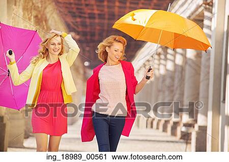 Stock Image - Self-confident girls walking with colorful umbrellas. Fotosearch