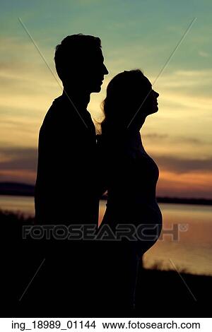 Picture - Silhouette of the man hugging his pregnant girlfriend. Fotosearch