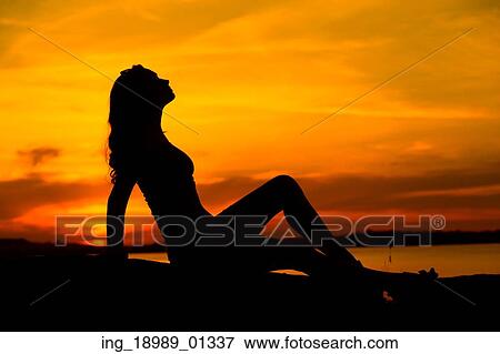 Stock Photo - Silhouette of the pregnant lady sitting on the sand. Fotosearch