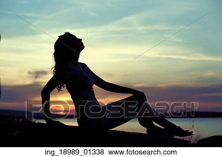 Stock Photo - Silhouette of the young lady sitting close to the sea. Fotosearch