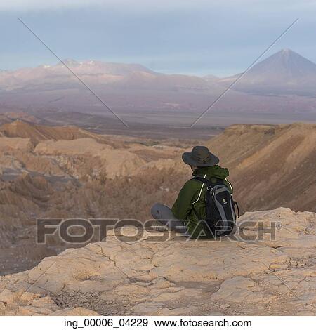 Stock Photo - Tourist sitting on edge of cliff, Death Valley, San Pedro de Atacama, El Loa Province, Antofagasta Region, Chile. Fotosearch