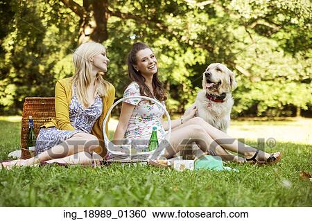 Stock Image - Two girlfriends with dog on the summer picnic. Fotosearch