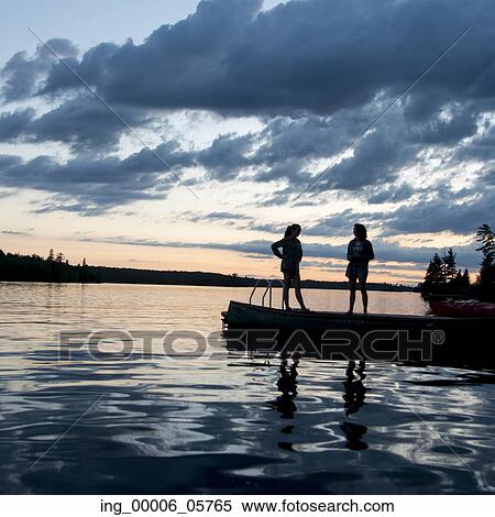Stock Photography - Two Woman standing on dock at dusk, Lake of the Woods, Ontario, Canada. Fotosearch