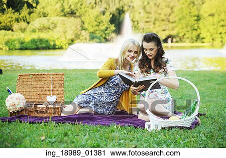 Stock Image - Two women reading book in the colorful park. Fotosearch