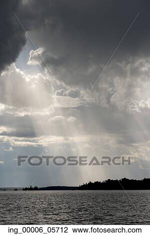 Stock Image - View of sunbeam through clouds over a lake, Lake of the Woods, Ontario, Canada. Fotosearch