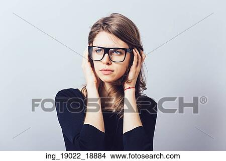 Picture - Woman in glasses, adjusts his glasses or hair on a grey background. Fotosearch
