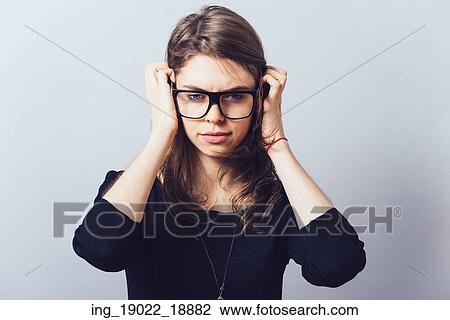 Stock Image - Woman in glasses, adjusts his glasses or hair on a grey background. Fotosearch