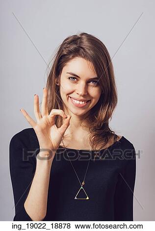 Stock Photo - Woman shows okay on a gray background.. Fotosearch