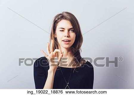 Stock Photograph - Woman shows okay on a gray background.. Fotosearch