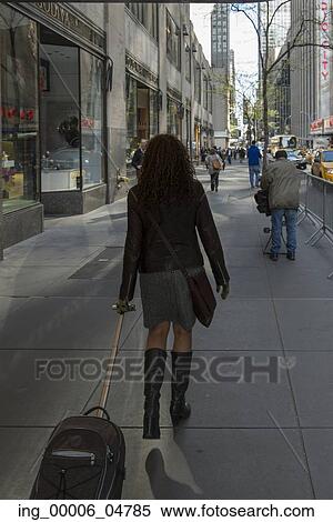Stock Photography - Woman with suitcase moving on a street, Manhattan, New York City, New York State, USA. Fotosearch