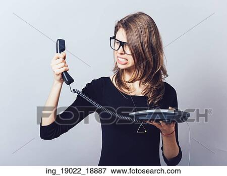 Stock Photo - Woman with the office or home phone swears, screams. On a gray background.. Fotosearch
