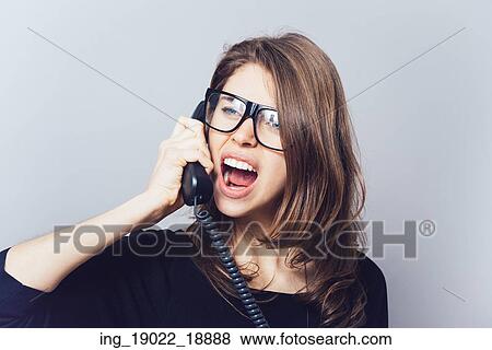 Stock Photo - Woman with the office or home phone swears, screams. On a gray background.. Fotosearch
