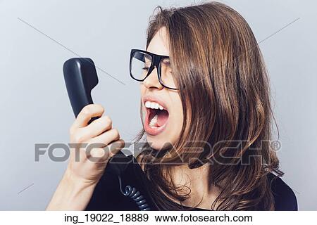 Woman with the office or home phone swears, screams. On a gray background. View Large Photo Image Stock Photo - Woman with the office or home phone swears, screams. On a gray background.. Fotosearch