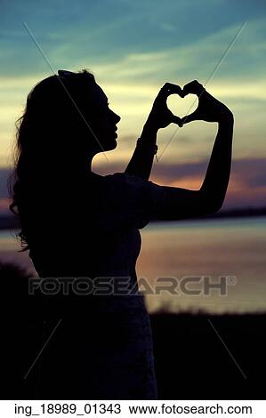 Stock Image - Woman&rsquo; s silhouette making the cute heart gesture. Fotosearch