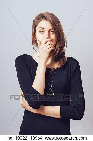 young adult woman holding hand over her mouth over grey background View Large Photo Image Picture - young adult woman holding hand over her mouth over grey background. Fotosearch