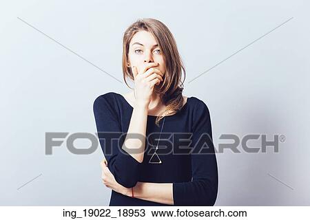 Stock Image - young adult woman holding hand over her mouth over grey background. Fotosearch
