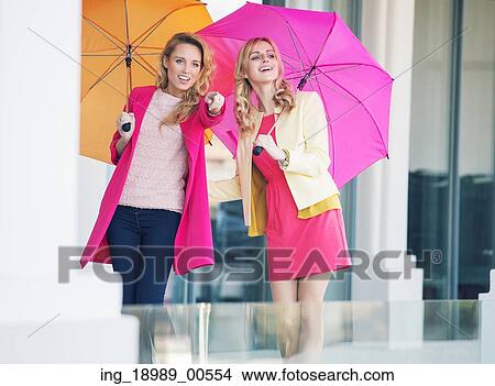 Picture - Young attractive girlfriends with the colorful umbrellas. Fotosearch