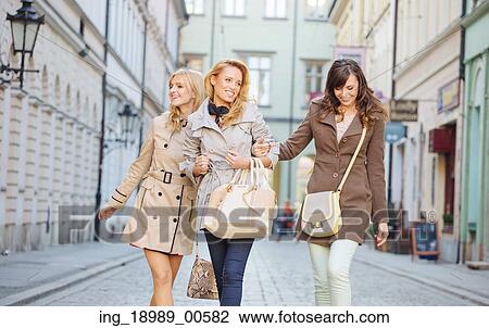 Stock Image - Young laughing girlfriends walking around the old town. Fotosearch
