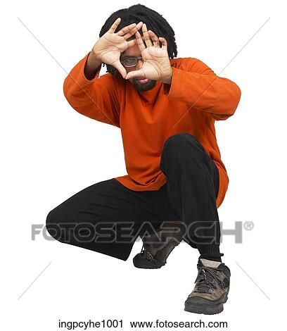 Stock Image - Young African American crouching on his heels making a triangle with his hands. Fotosearch