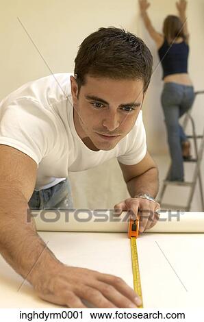 Close-up of a young man measuring a roll of wallpaper with a woman on a step ladder behind him View Large Photo Image Stock Image - Close-up of a young man measuring a roll of wallpaper with a woman on a step ladder behind him. Fotosearch