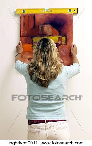 Rear view of a young woman hanging a painting on a wall View Large Photo Image Stock Image - Rear view of a young woman hanging a painting on a wall. Fotosearch