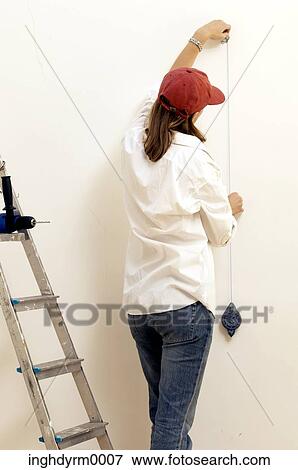 Stock Photo - Rear view of a young woman measuring a wall. Fotosearch
