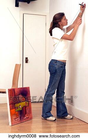 Side profile of a young woman hammering a nail into a wall View Large Photo Image Stock Photo - Side profile of a young woman hammering a nail into a wall. Fotosearch