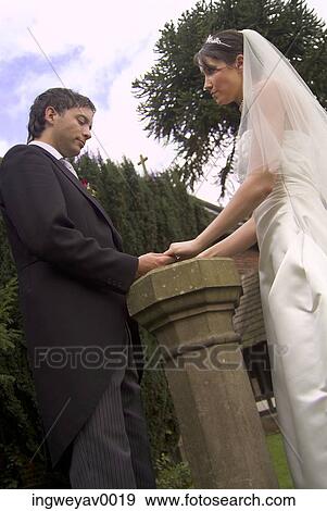 Stock Photo - Low angle view of a young bride and groom holding hands in a garden. Fotosearch