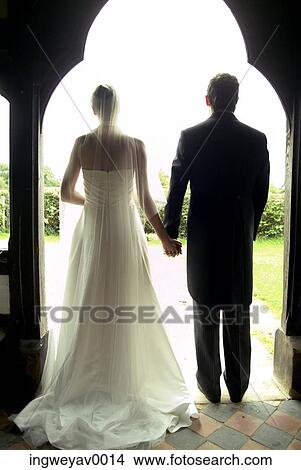 Rear view of a young bride and groom holding hands in a doorway View Large Photo Image Picture - Rear view of a young bride and groom holding hands in a doorway. Fotosearch