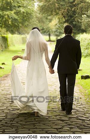 Rear view of a young bride and groom walking in a garden View Large Photo Image Stock Photo - Rear view of a young bride and groom walking in a garden. Fotosearch