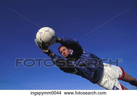 Picture - Low angle view of a male goalie jumping to stop a ball. Fotosearch