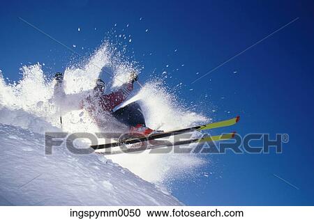 Stock Image - Low angle view of a skier throwing up snow while skiing on a mountain. Fotosearch