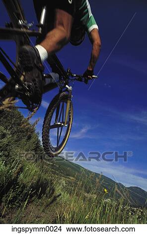 Low angle view of a young man riding a bicycle on a hilly trail View Large Photo Image Picture - Low angle view of a young man riding a bicycle on a hilly trail. Fotosearch