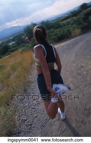 Stock Image - Rear view of a woman exercising on a dirt path. Fotosearch