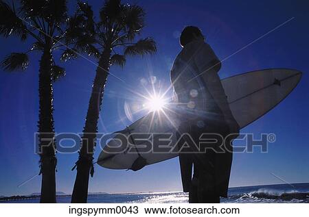 Silhouette of a man holding a surfboard standing on a beach View Large Photo Image Stock Image - Silhouette of a man holding a surfboard standing on a beach. Fotosearch