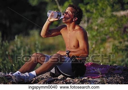 Young man drinking water sitting outdoors View Large Photo Image Stock Image - Young man drinking water sitting outdoors. Fotosearch