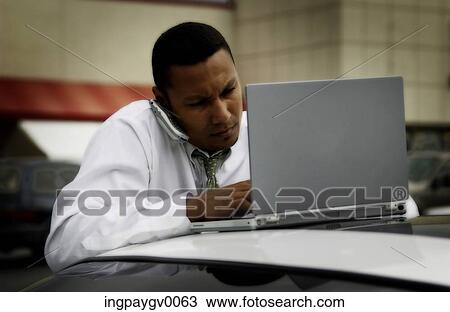 A mid adult businessman talking on a mobile phone and working on a laptop computer View Large Photo Image Stock Image - A mid adult businessman talking on a mobile phone and working on a laptop computer. Fotosearch