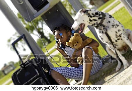 Stock Photograph - A young girl talking on a pay phone with a Dalmatian by her side. Fotosearch