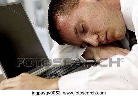Stock Image - Close-up of a young businessman lying asleep next to a laptop computer. Fotosearch