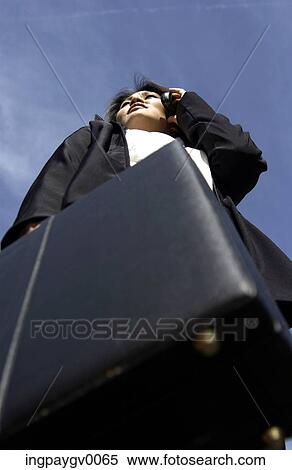 Low angle view of a businesswoman holding a briefcase, talking on a mobile phone View Large Photo Image Stock Photography - Low angle view of a businesswoman holding a briefcase, talking on a mobile phone. Fotosearch