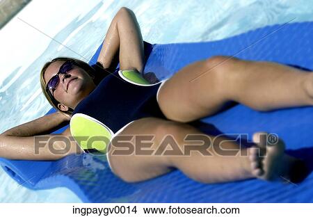 Picture - Low angle view of a young woman wearing a swim suit, lying on a raft in a swimming pool. Fotosearch