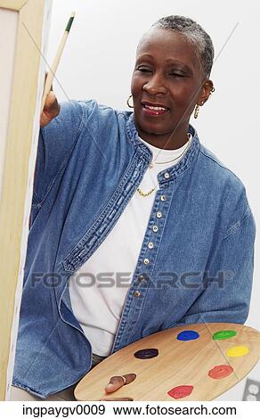 Mature woman holding a palette, sitting in front of a painting canvas View Large Photo Image Stock Photo - Mature woman holding a palette, sitting in front of a painting canvas. Fotosearch