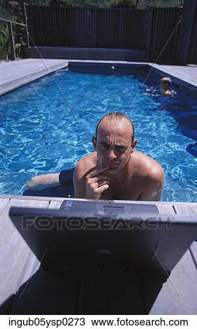 Stock Image - High angle view of a young man in a swimming pool using a laptop. Fotosearch