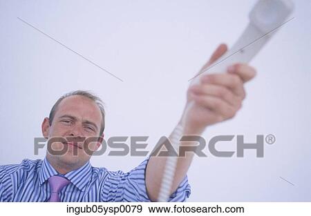 Low angle view of a businessman holding out a telephone receiver View Large Photo Image Stock Photo - Low angle view of a businessman holding out a telephone receiver. Fotosearch
