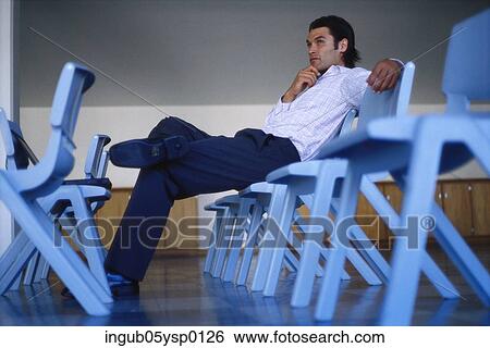Low angle view of a young man sitting on a chair View Large Photo Image Stock Photograph - Low angle view of a young man sitting on a chair. Fotosearch
