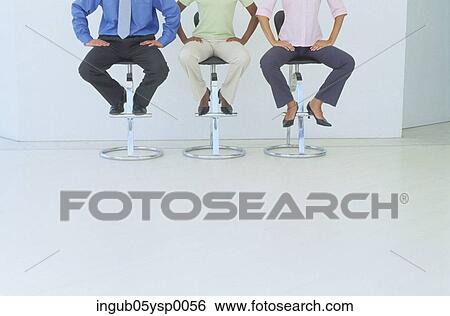 Stock Photograph - Low-section view of two young women and a young man sitting on stools. Fotosearch