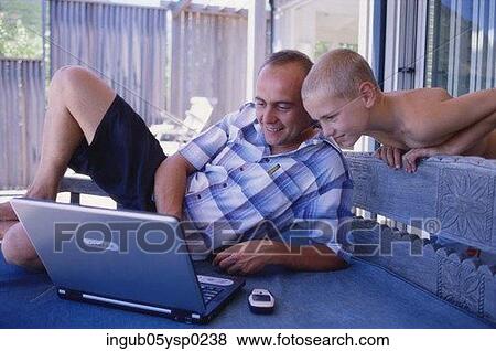 Stock Photo - Mid adult man and his son looking at a laptop. Fotosearch