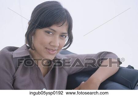 Portrait of a young woman sitting on a couch View Large Photo Image Stock Image - Portrait of a young woman sitting on a couch. Fotosearch