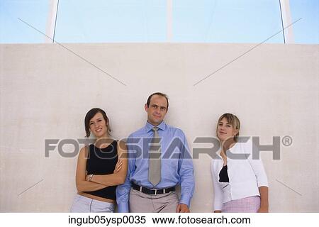 Stock Photography - Portrait of two young women and a young man leaning on a wall. Fotosearch