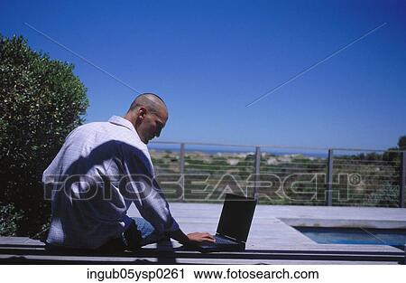 Rear view of a young man sitting at a poolside with a laptop View Large Photo Image Stock Image - Rear view of a young man sitting at a poolside with a laptop. Fotosearch
